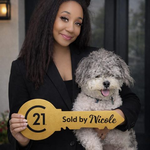 Nicole McGowan holding a gold CENTURY 21 'Sold by Nicole' key sign with her dog Bentley