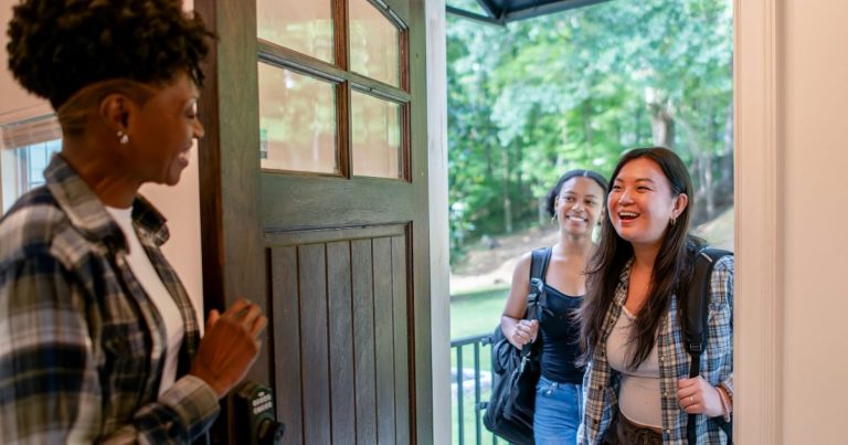 Smiling woman opening her front door to welcome two visitors to an open house